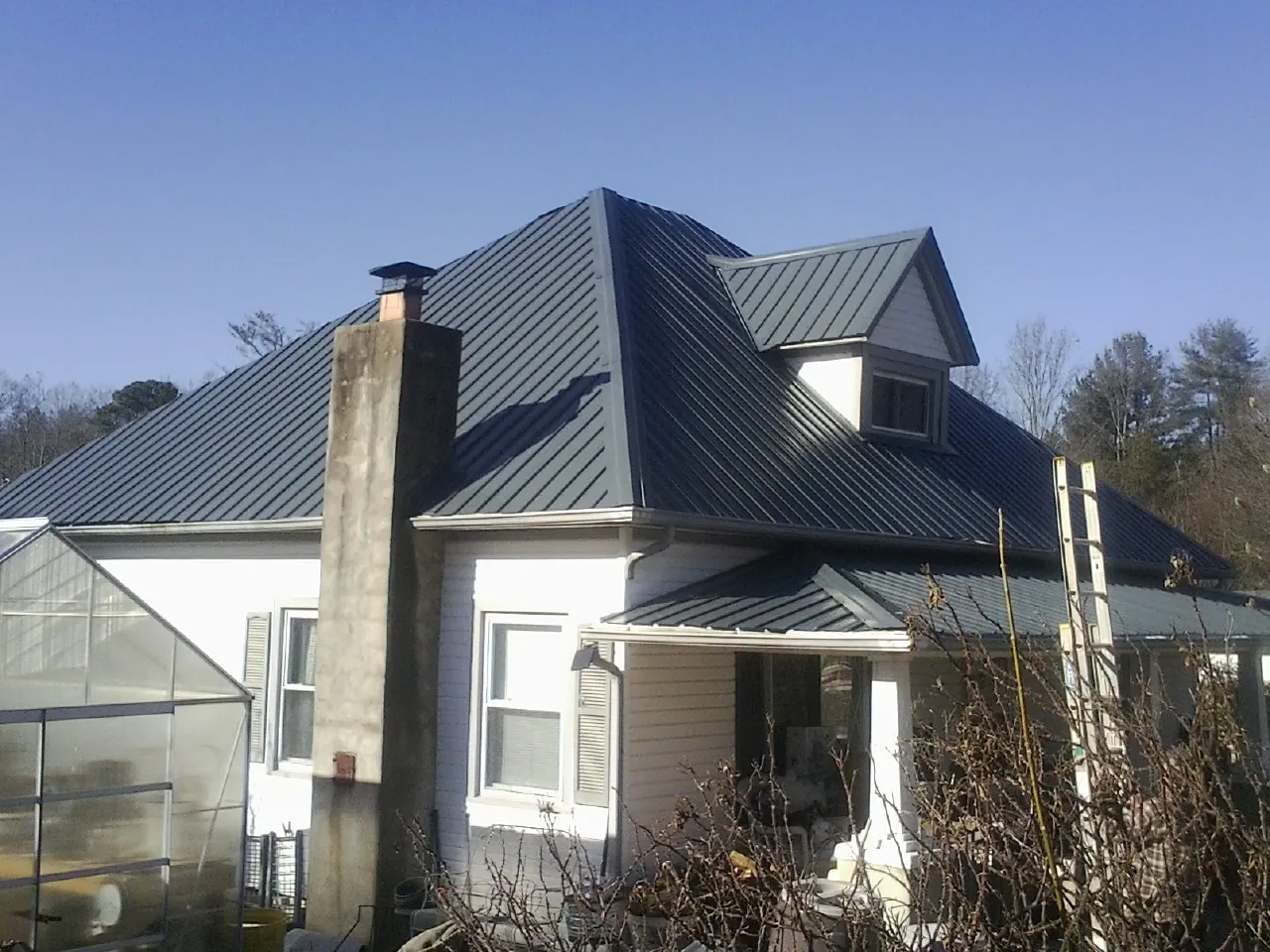 Dark blue standing seam metal roof on a white farmhouse with dormer — Slate & Tile Roof Repair by Roofing Brothers in Tecumseh