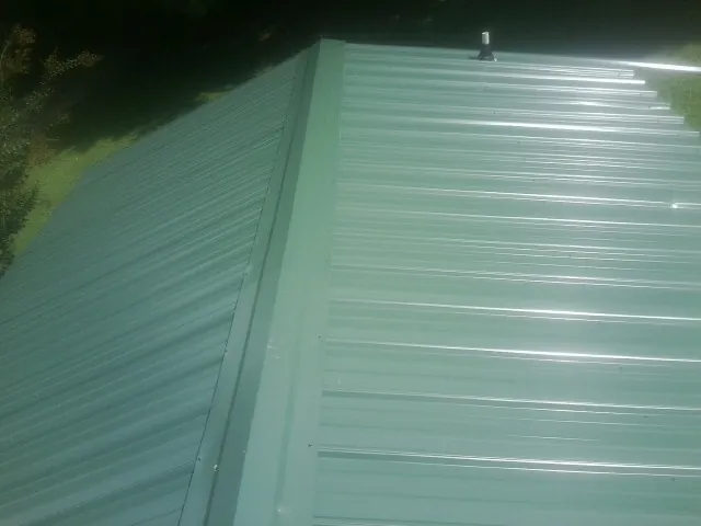 New green metal panels meeting at the ridge of a roof — Flat Roof Repair work by our crew in Tecumseh