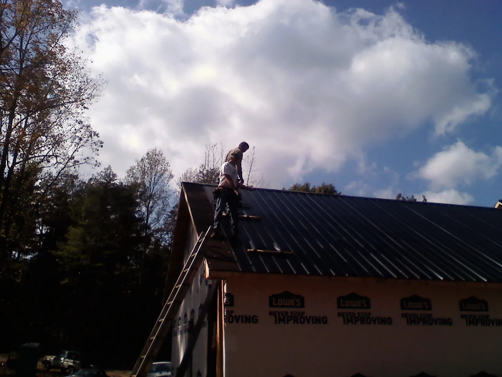 Roofer fastening dark metal panels high against a cloudy sky, from a Roof Inspection job in Tecumseh